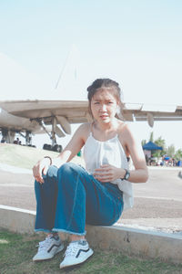 Full length of young woman sitting by airplane at airport