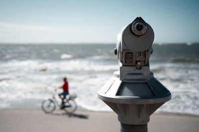 Coin-operated binoculars by sea against sky