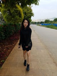 Portrait of smiling young woman standing on footpath