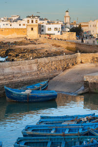 Boats moored on sea by buildings against blue sky