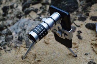 High angle view of mobile phone with lens at beach