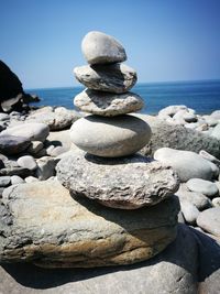 Stack of pebbles at beach against clear blue sky during sunny day