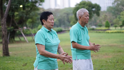 Senior couple exercising while standing on field against trees