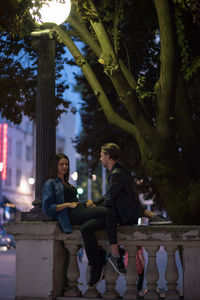 Portrait of young couple sitting on illuminated tree at night