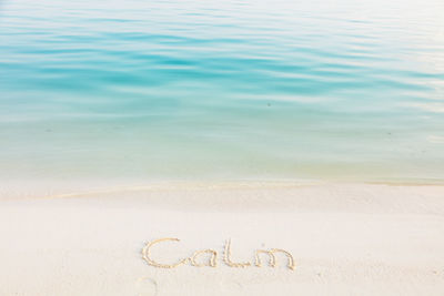The word calm written in the sand on a beach with blue sea background