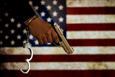 Cropped hand with handcuffs holding gun against american flag