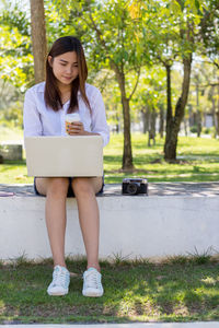 Young woman using mobile phone while sitting on tree