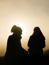 Silhouette couple sitting against clear sky during sunset