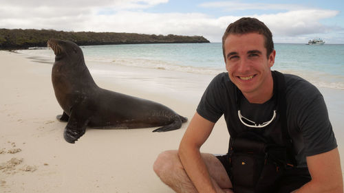 Portrait of smiling man with sea lion at beach against sky