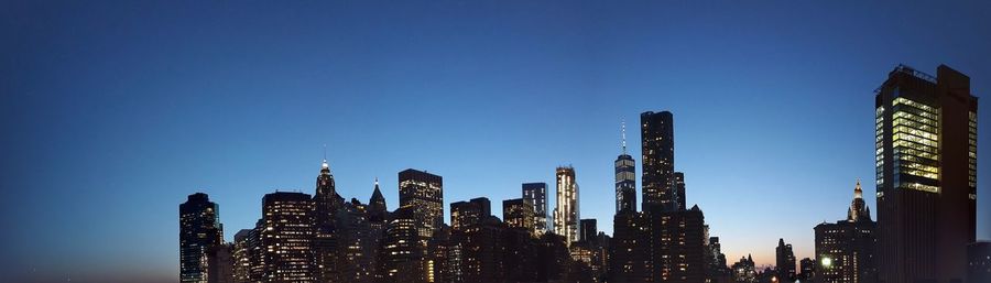 Low angle view of skyscrapers lit up against blue sky