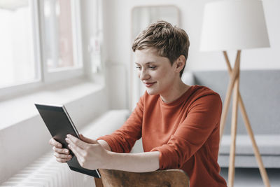 Smiling woman sitting on chair using tablet