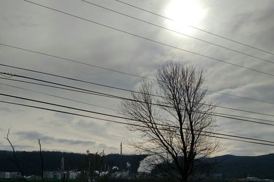 Low angle view of electricity pylon against cloudy sky