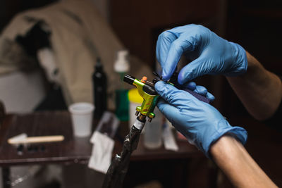 Side view of crop tattooist in protective gloves holding professional tattoo machine while working in salon