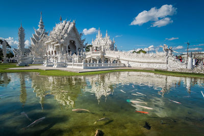 Pond by wat rong khun against sky