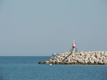 Lighthouse by sea against clear sky