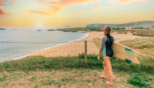 Rear view of woman standing at beach against sky during sunset