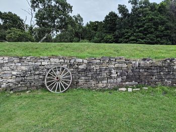 Stone wall by trees on field against sky