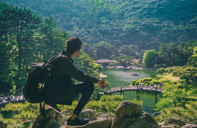 Backpacker sitting on rock while looking at mountains and river