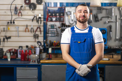 Handsome young man auto mechanic in special uniform clothes is standing and smiling 