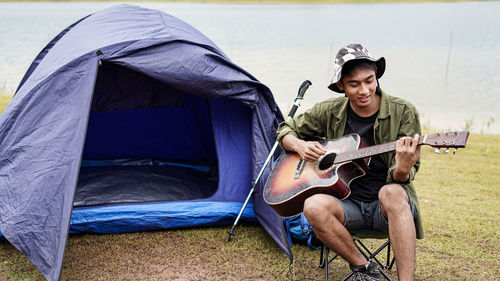 Man playing guitar while camping against clear sky