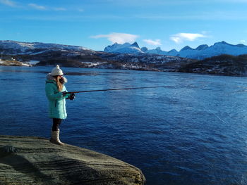 Rear view of woman standing in sea against mountains