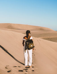 Rear view of woman standing on sand dune in desert against clear sky