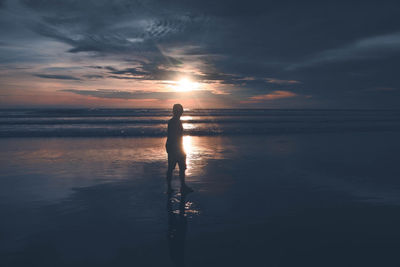 Silhouette man standing at beach against sky during sunset