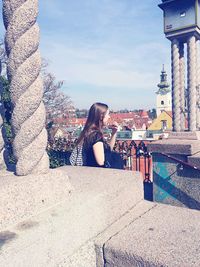 Woman sitting on retaining wall against sky