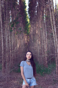 Portrait of young woman standing against tree in forest