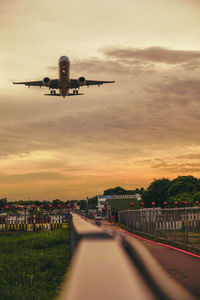 Airplane flying over city against sky during sunset