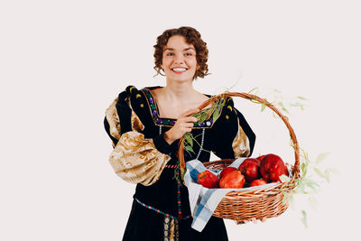 Portrait of smiling young woman in wicker basket against white background