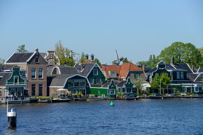 Houses by river and buildings against clear blue sky