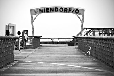 Text on entrance at wooden bridge against clear sky