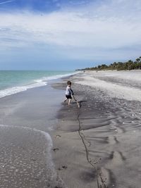 Full length of boy playing on shore at beach against sky