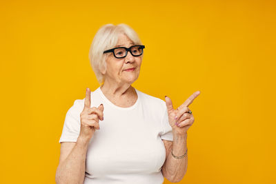 Portrait of young woman with arms raised against yellow background