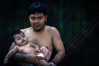 Portrait of shirtless father carrying son