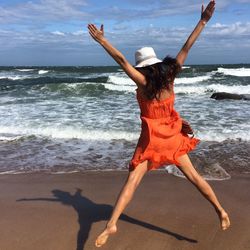 Full length of woman in mid-air at beach against sky