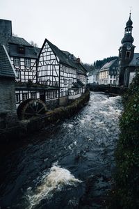 Bridge over river by houses against sky