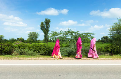Women walking on road by trees against sky