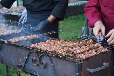 Midsection of men arranging kebab skewers on barbecue grill