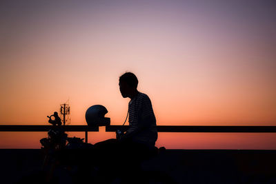 Silhouette people sitting against orange sky