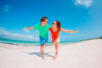 Full length of friends enjoying at beach against blue sky