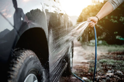 Cropped hand spraying water on car at field