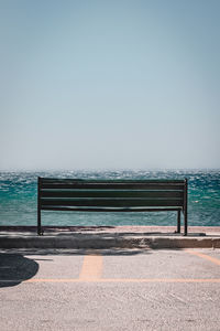 Empty bench on beach against clear sky