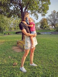 Woman with a face mask, holding her child in a park. 