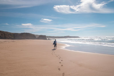 Rear view of woman walking at beach against sky