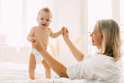 A smiling little child learns to walk and holds her mother's hands. the concept of family, child.