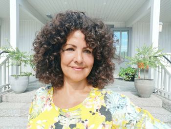 Smiling mature woman with curly hair against house