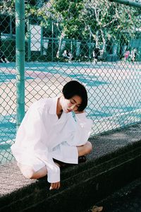 Young woman sitting on retaining wall by basketball court