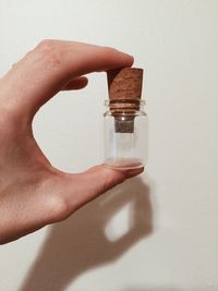 Cropped hand of person holding glass bottle against wall